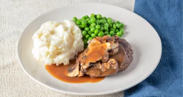 Plate of meatloaf with mushroom gravy, mashed potatoes and peas