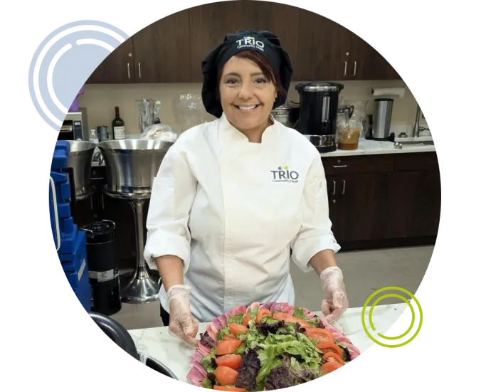 Chef standing in kitchen smiling while behind a food display