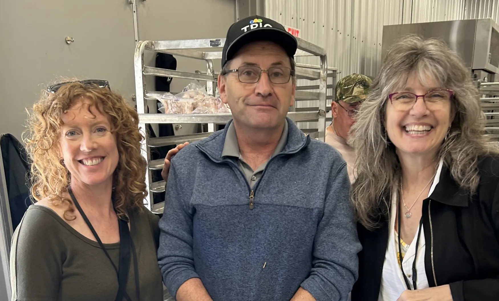 Three employees smiling with food racks in background