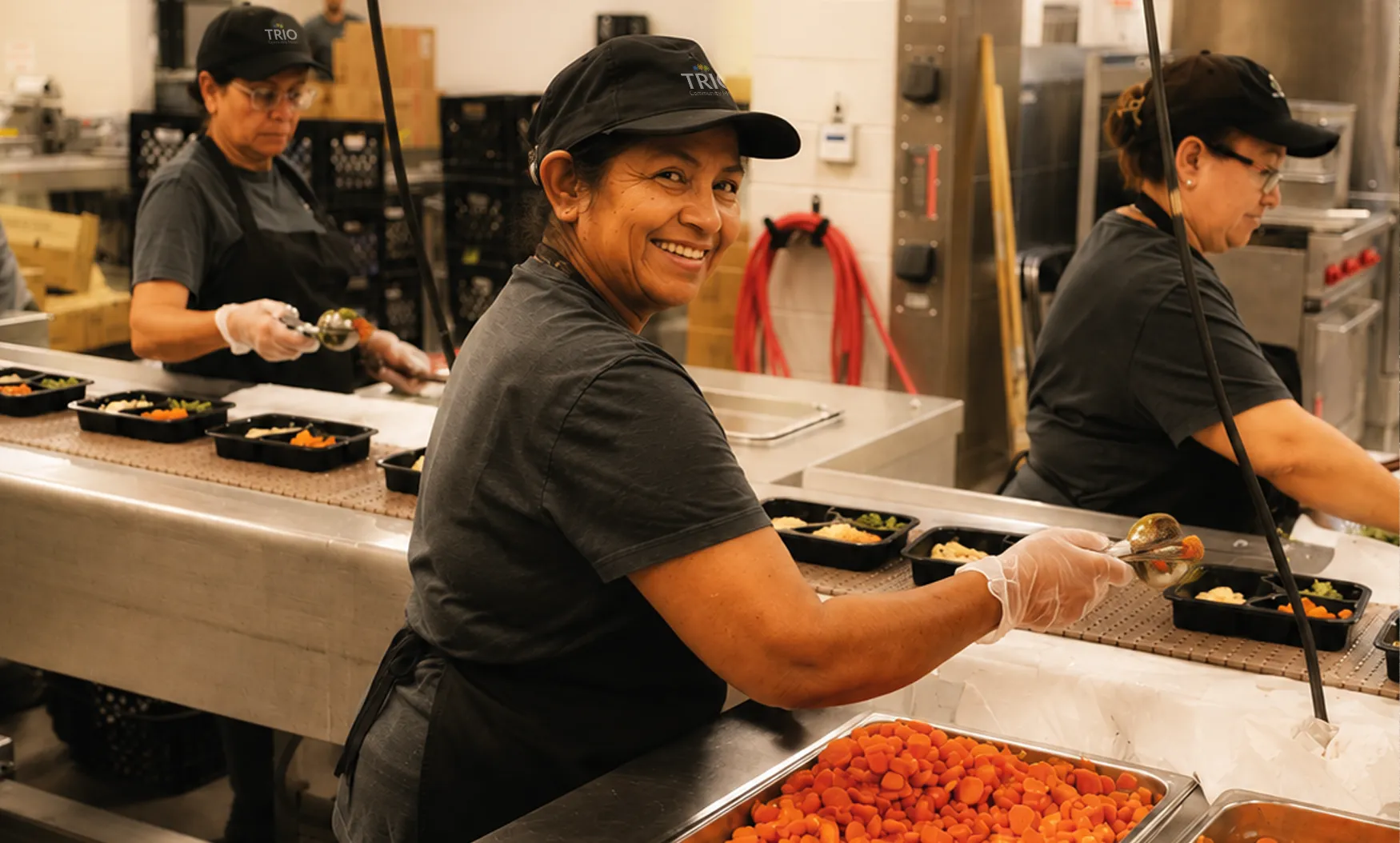 happy kitchen employee scooping vegetables on food tray line
