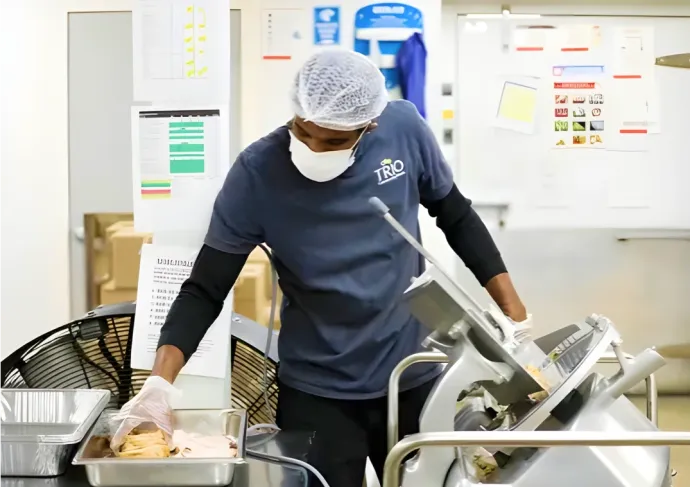 Employee placing food into tray while standing behind slicer