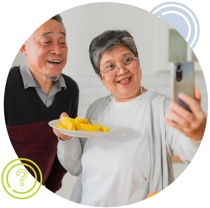 Two adults smiling while on cell phone, one holding a plate of fruit