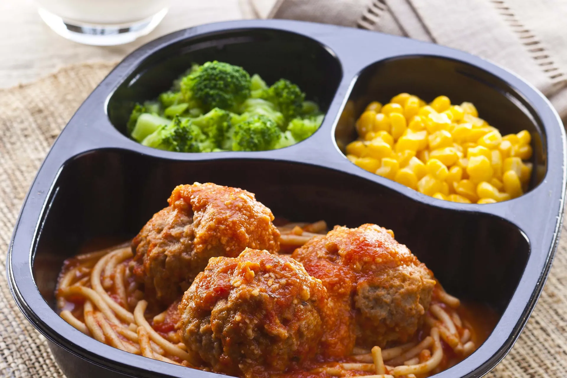 Spaghetti and meatballs, corn and broccoli in a microwavable container