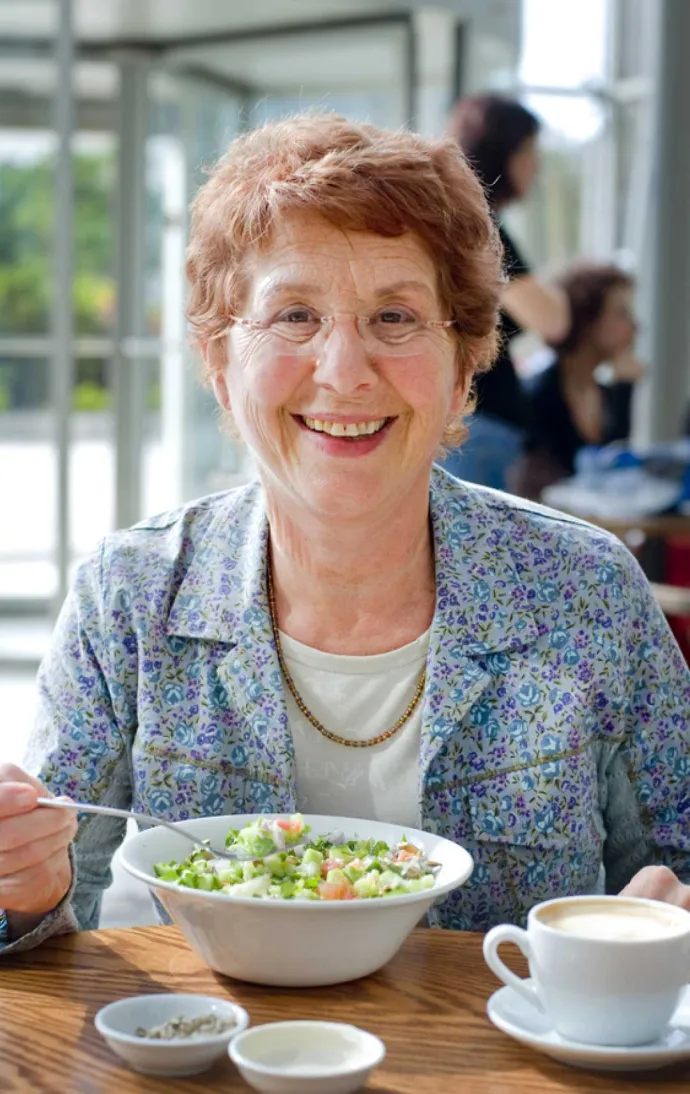 Senior woman smiling while eating a salad bowl at table