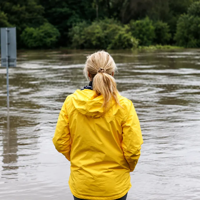 Woman in yellow rain coat overlooking a flooded area